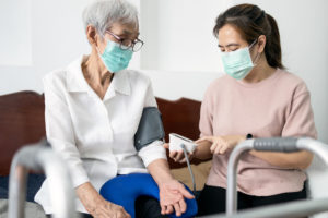 מטפלת מודדת לקשישה לחץ דם בעידן הקורונה (עם מסיכות)